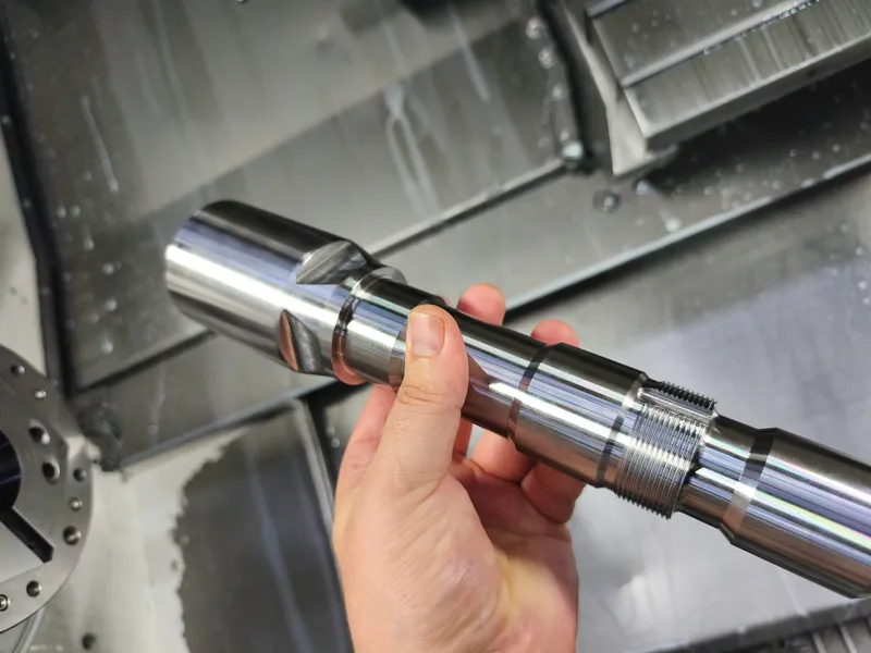 Turned shaft with shoulders and thread held in front of the machine